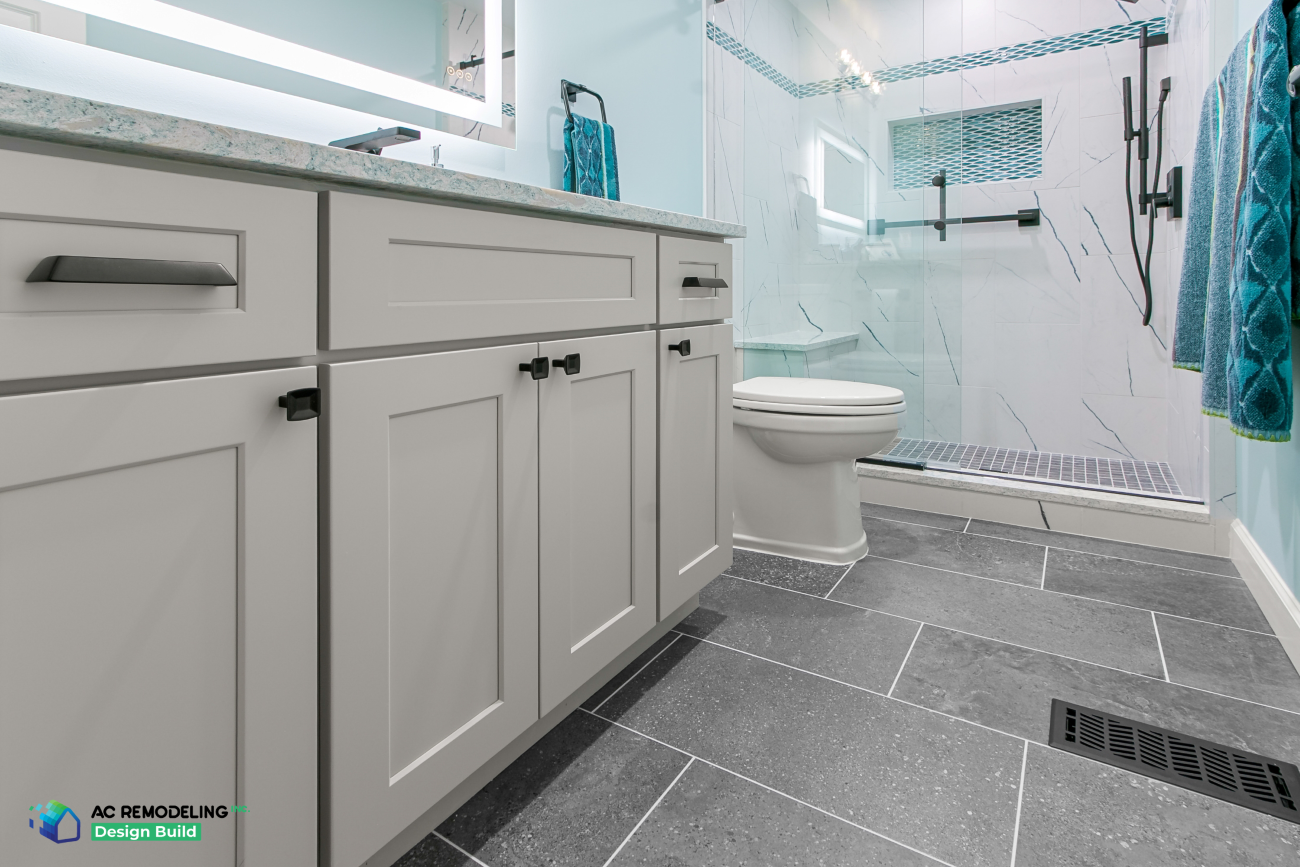Gray shaker vanity with matte black hardware, slate-look tile floor and glass shower beyond