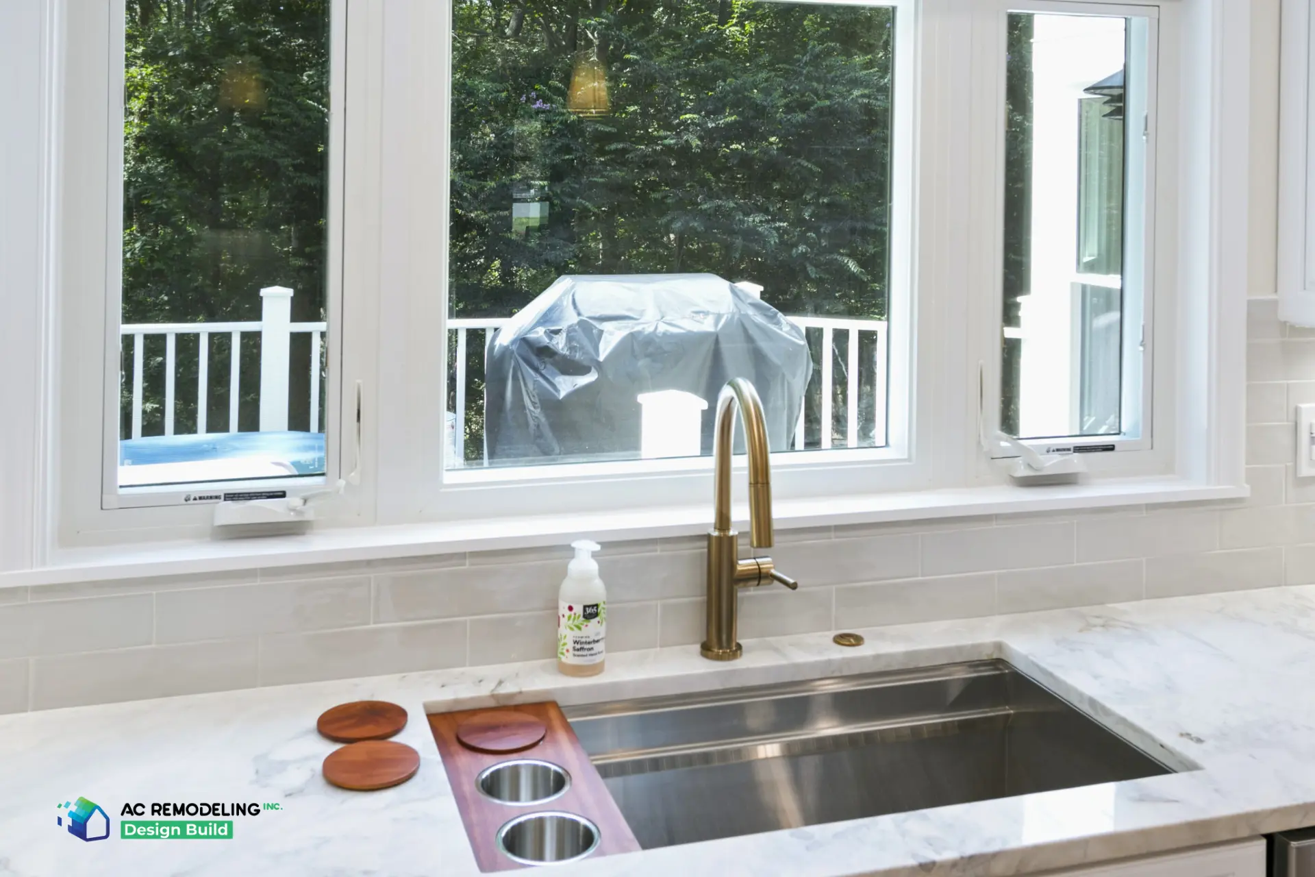 Workstation sink with walnut board and brass faucet framed by windows