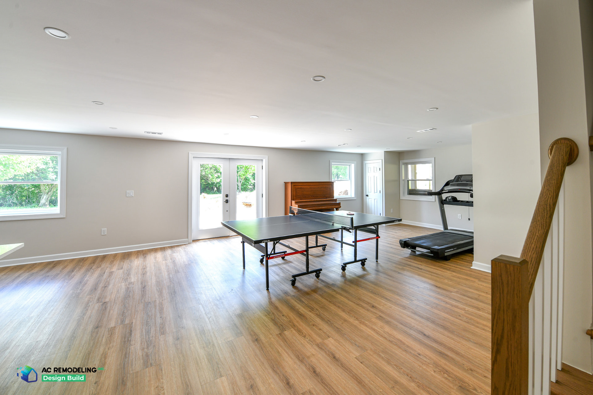 Bright finished basement recreation room with ping-pong table, treadmill, piano and exterior doors