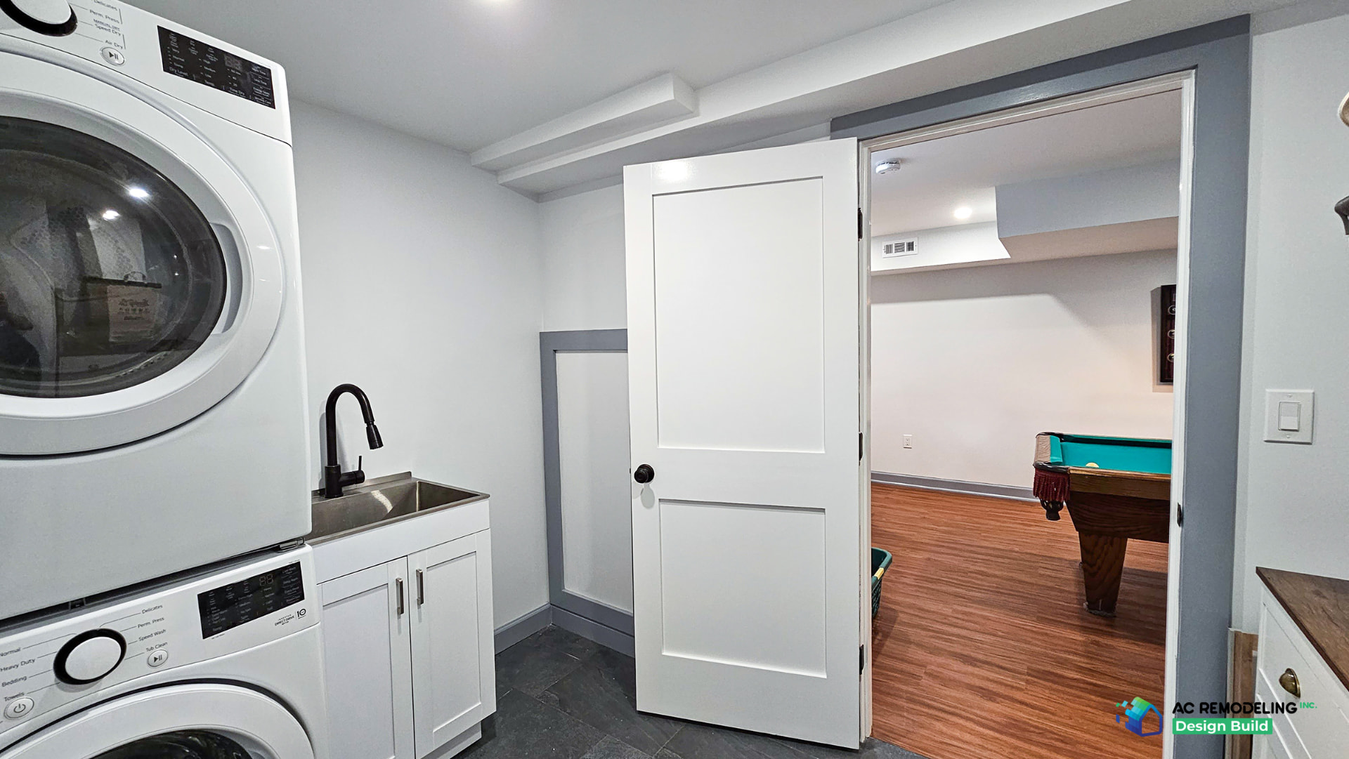 Basement laundry room with stacked washer and dryer, utility sink, white cabinetry and dark tile floor