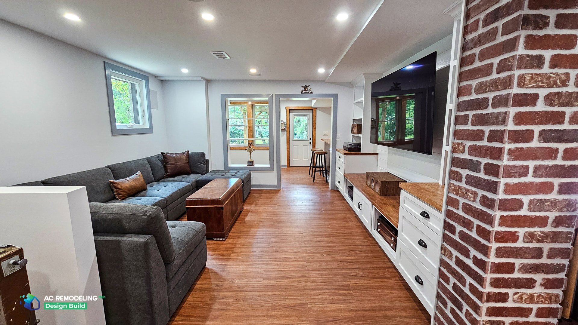 Finished basement media lounge with gray sectional, custom cabinetry, wood flooring and exposed brick column