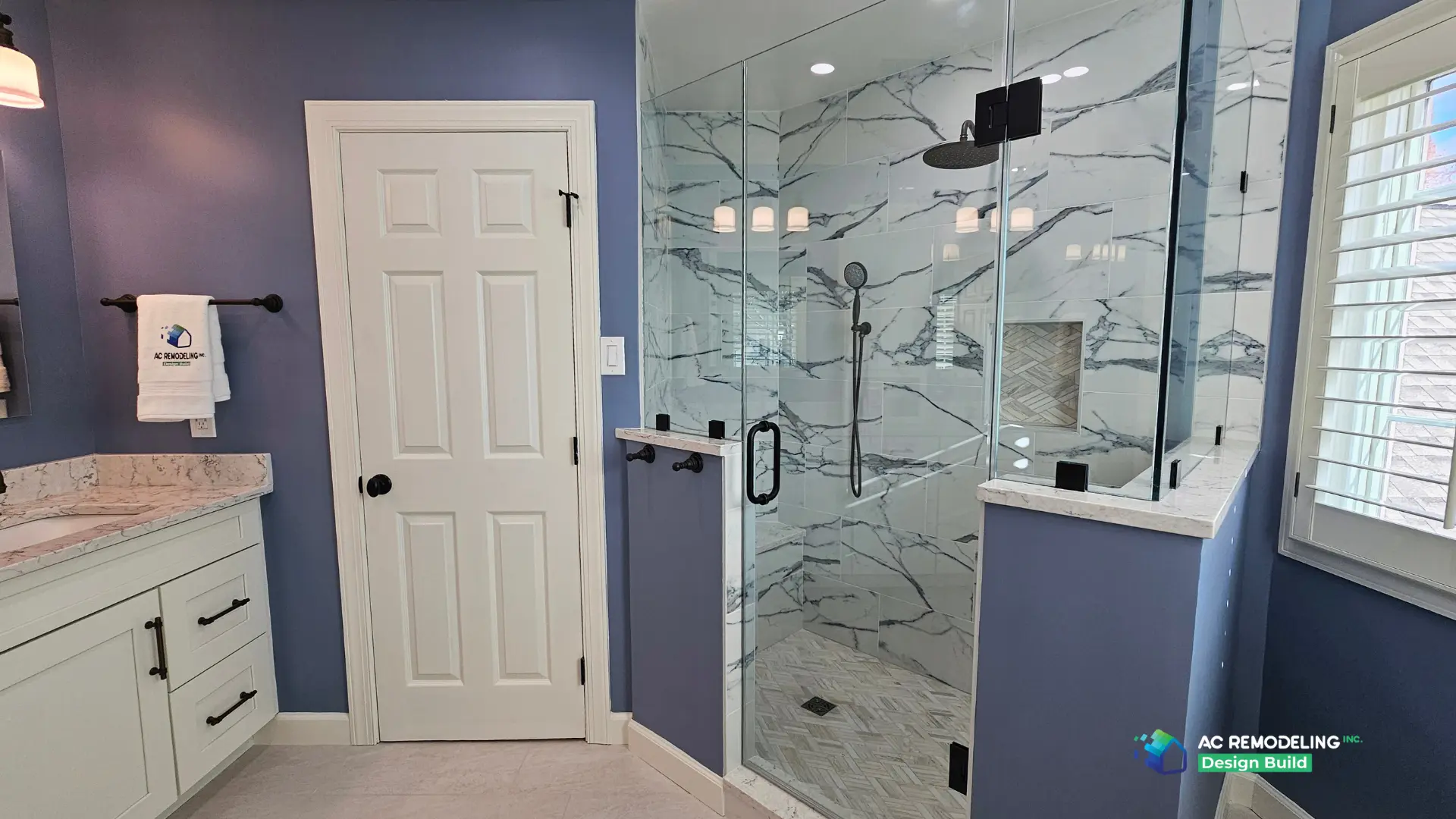 Frameless glass shower with marble-look slab tile, rain head and herringbone floor