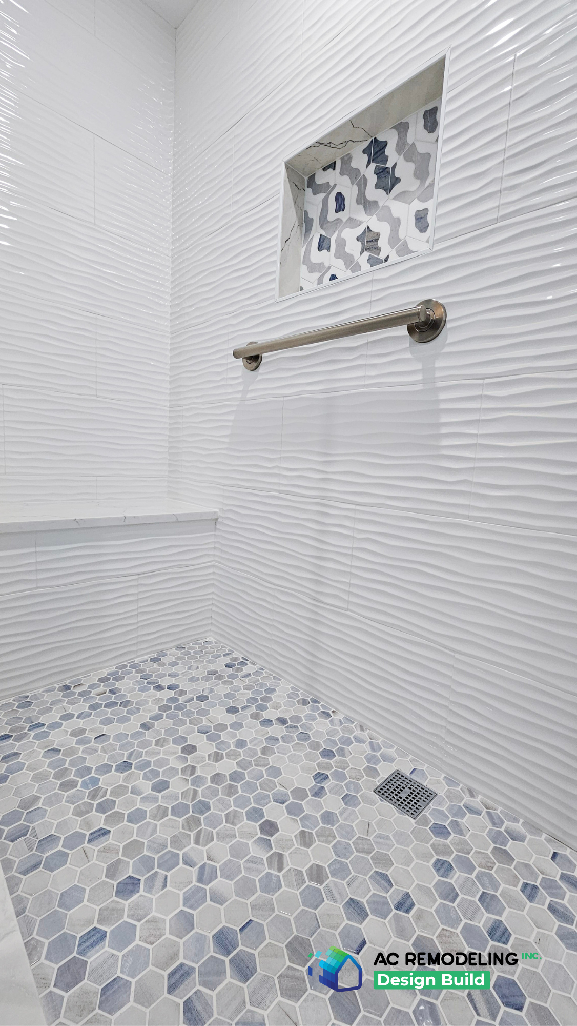 Shower interior with wave-texture white tile, quartz bench, grab bar and blue hex mosaic floor