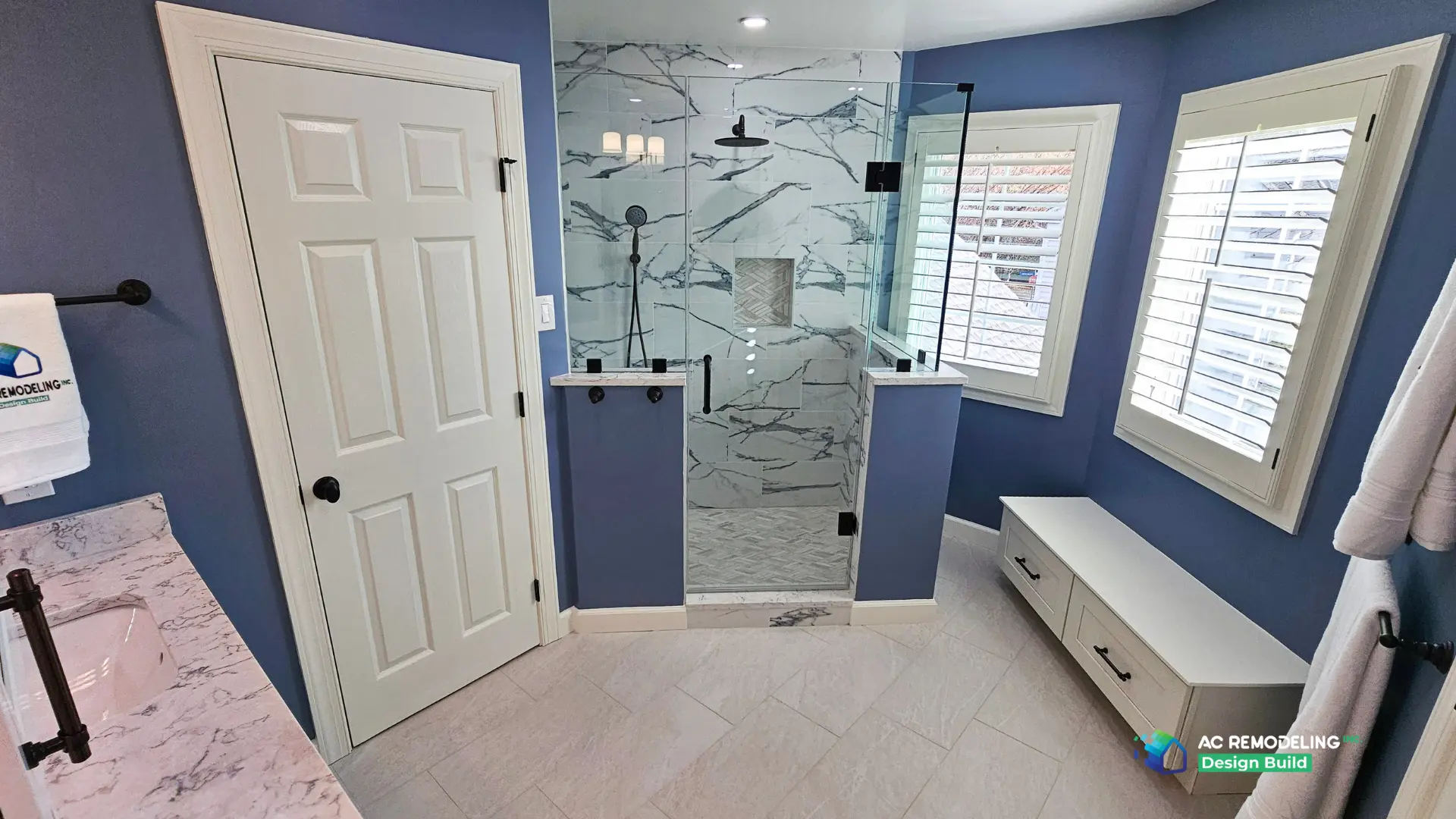Corner shower with rain head, herringbone floor and a built-in drawer bench beneath shuttered windows