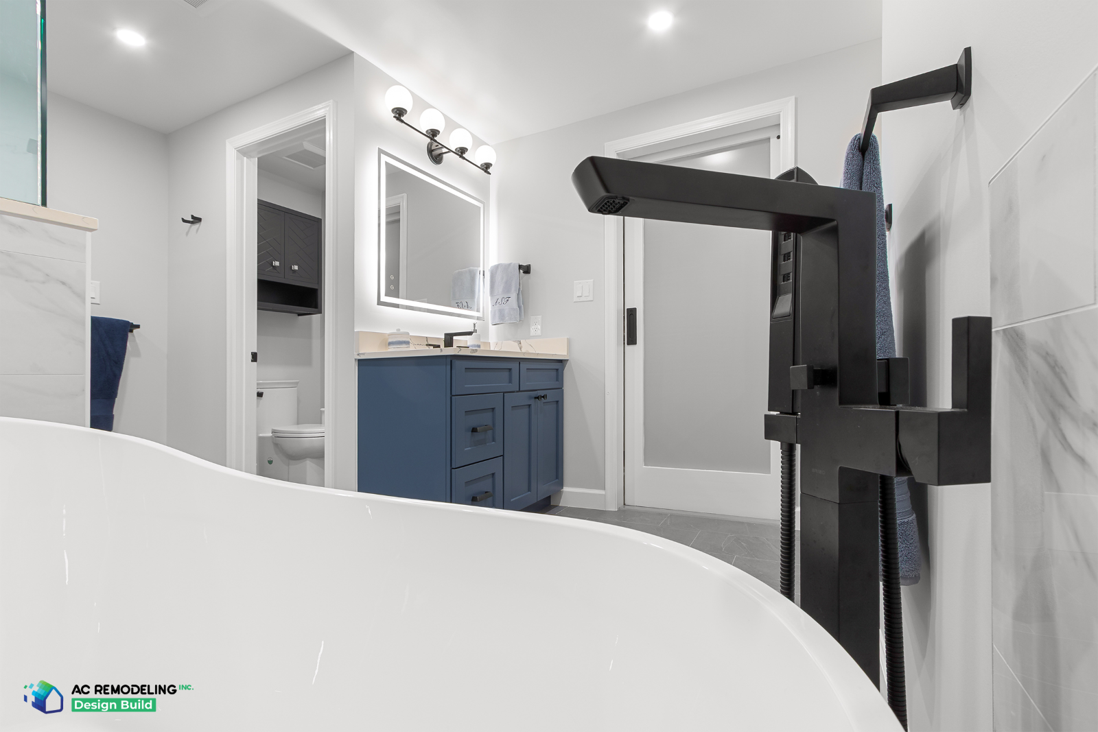 Primary suite bath with soaking tub, navy vanity and water closet beyond