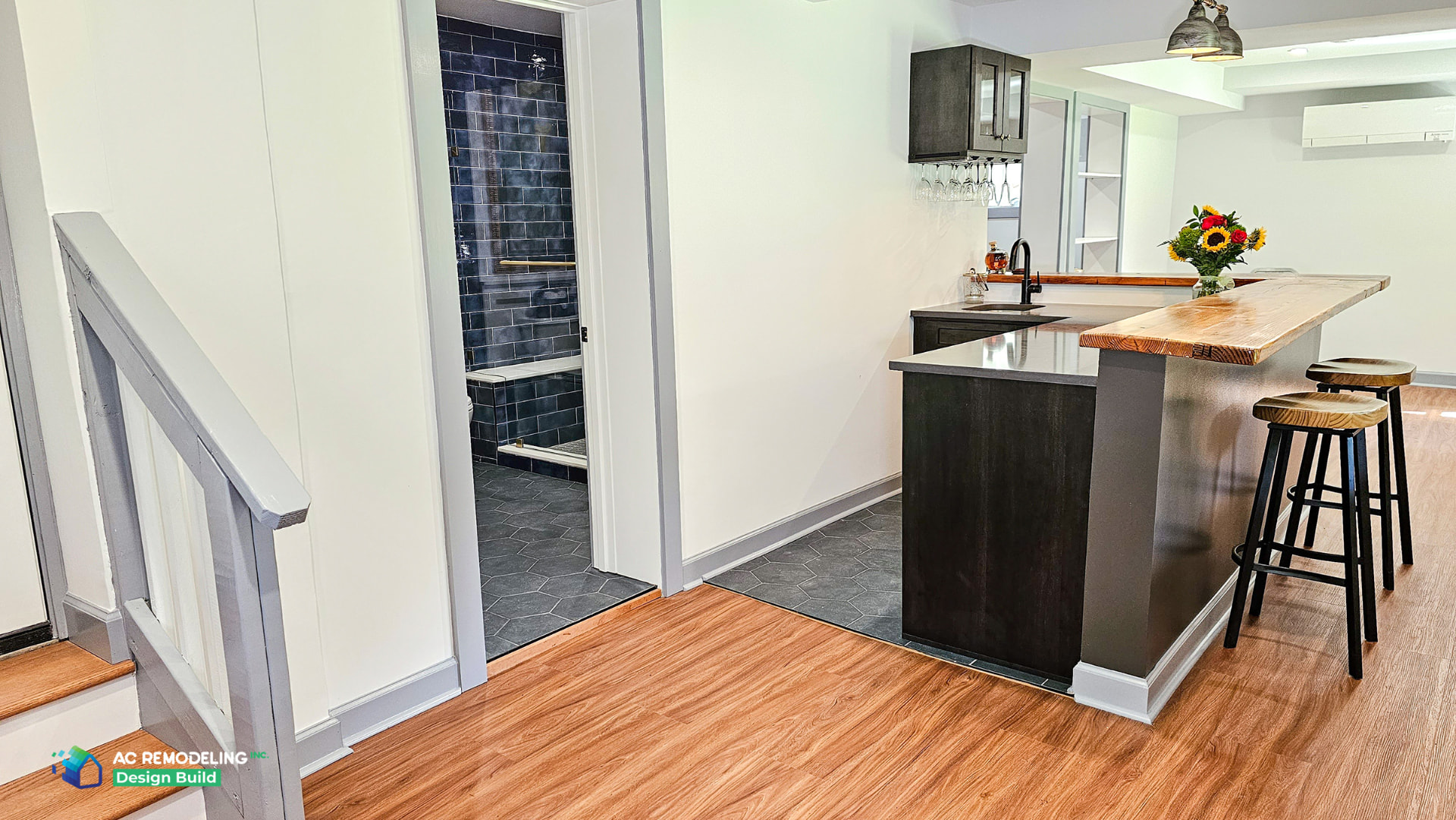 Basement bar with wood counter, dark cabinetry and view into the blue-tiled bathroom
