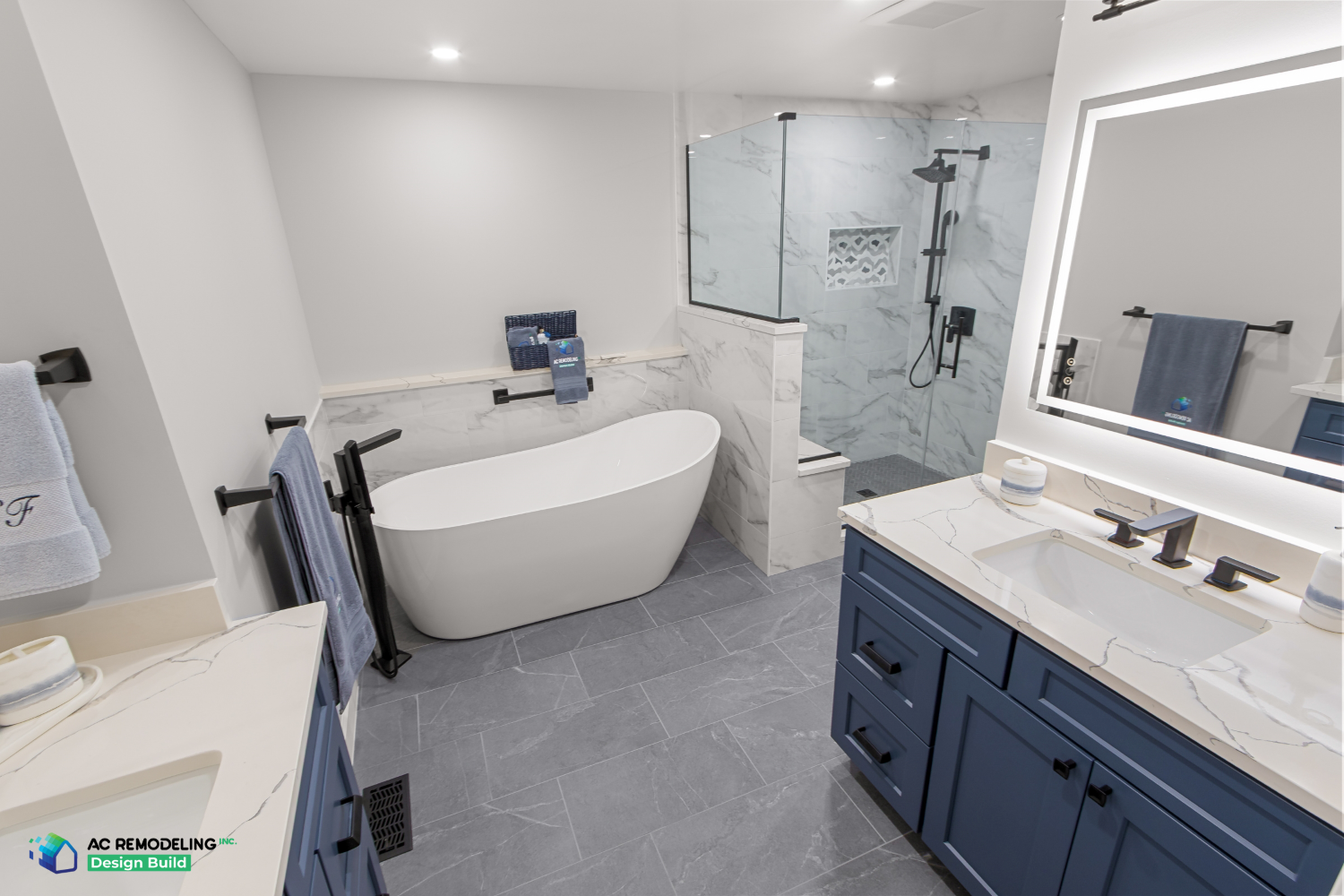 Primary bath with freestanding soaking tub, marble-tiled walk-in shower and navy vanities with backlit mirror